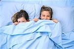 Sisters in Bed, Peeking From Under Blankets