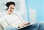 Man Using Laptop Computer, Listening to Headphones