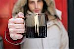 Mann in einem Mantel hält eine Kaffeetasse