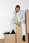 Businessman Using Telephone While Sitting on Boxes