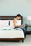 Man Sitting on Edge of Bed with Laptop Computer and Credit Card