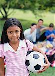 Girl Holding Soccer Ball and Family Having Picnic