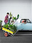 Woman Watching Man Loading Plants Into Trunk of Car