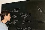 Young man contemplating equation on blackboard