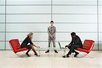 Two Business People using Laptops, with Businessman Standing by Wall