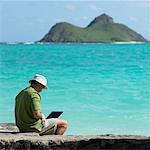Homme assis sur un rocher de l'océan, ordinateur portable à l'aide, Oahu, Hawaii