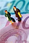 Toy businessman and businesswoman standing on top of Euro bank notes