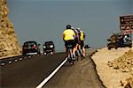 Rear view of three people riding cycles on a road