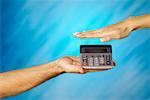 Close-up of a man holding a calculator with a woman's hand above it