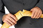 Mid section view of a businessman breaking a loaf of bread