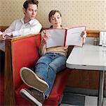 Young Women Reading Menu in Diner, With Man Peeking Over Shoulder