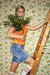 Woman Standing on Ladder, Holding Plant