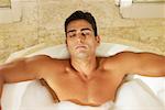 High angle view of a bare chested young man lying in a bathtub with his eyes closed