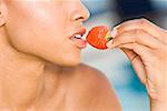 Close-up of a young woman holding a strawberry close to her mouth