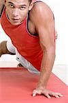 Portrait of a young man doing one hand push-ups on an exercise mat