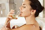 Profil de côté d'une jeune femme à boire du vin blanc dans une baignoire
