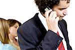 Businessman talking on a mobile phone with his two secretaries standing behind him