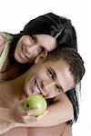 Portrait of a young woman holding a green apple embracing a young man from behind