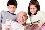 Grandfather reading a newspaper with his grandson and his granddaughter