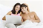 Junges Paar sitzt auf einem Bett, Blick auf einen laptop
