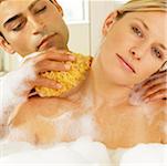 Gros plan d'un jeune homme frotter le cou d'une jeune femme avec une éponge de bain