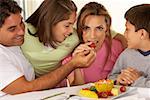 Mitte erwachsener Mann Fütterung einer Frau der mittleren Alters eine Erdbeere mit ihren beiden Kindern neben Ihnen