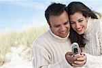 Couple Looking At Photo On Cell Phone At The Beach