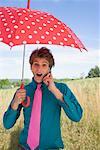 Young Man Using Cell Phone and Holding Umbrella