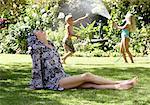 Grandmother Lounging While Kids Play With Hose in Backyard