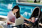 Mother using a laptop with her daughter beside her at the poolside