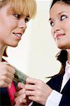 Side profile of two businesswomen holding a dollar bill