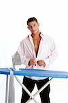 Portrait of a young man standing in front of an ironing board and buttoning his shirt