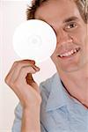 Portrait d'un homme adult moyen couvrant ses yeux avec un CD