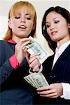Low angle view of a businesswoman giving a dollar bill to another businesswoman