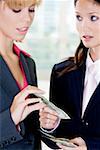 Close-up of a businesswoman giving a dollar bill to another businesswoman