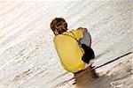 Rear view of a boy squatting on the beach