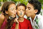 Close-up of two boys and a girl blowing bubbles with a bubble wand