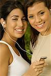 Portrait of two teenage girls holding an MP3 player listening to music