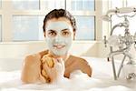 Portrait d'une jeune femme avec un masque facial tenant une éponge de bain