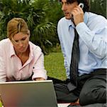 Close-up of a businessman talking on a mobile phone with a businesswoman using a laptop