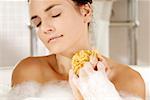 Close-up of a young woman with her eyes closed scrubbing her neck with a bath sponge