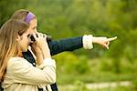 Side profile of a teenage girl pointing forward with a girl looking through a pair of binoculars