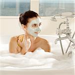 Gros plan d'une jeune femme avec un masque facial tenant une éponge de bain