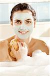 Portrait d'une jeune femme avec un masque facial tenant une éponge de bain et souriant