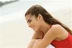 Profil de côté d'une jeune fille assise sur la plage souriant