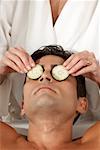 Mid section view of a massage therapist putting slices of cucumber on a young man's eyes