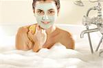 Portrait d'une jeune femme avec un masque facial tenant une éponge de bain dans une baignoire