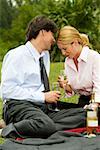 Businessman and a businesswoman sitting in the park holding champagne flutes