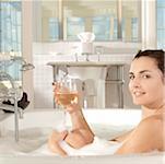 Portrait of a young woman holding a glass of a wine in a bathtub