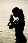 Side profile of a young woman in a prayer position in the lake